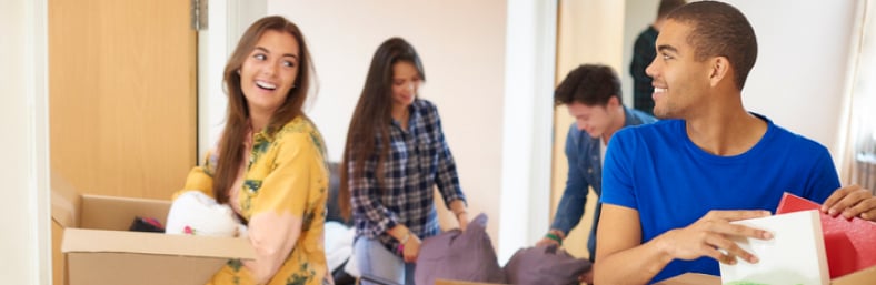 A group of students smile at each other while carrying and unpacking boxes during a campus move-in day.